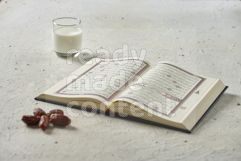 Quran with dates, prayer beads and different drinks all placed on textured white background