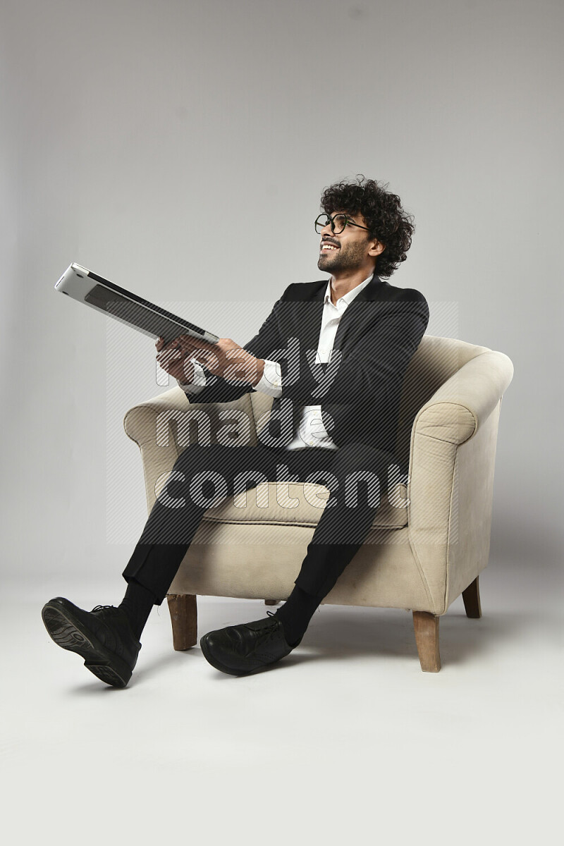 A man wearing formal sitting on a chair holding a laptop on white background