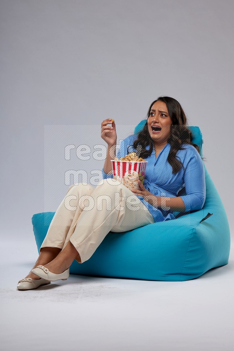 A woman sitting on a blue beanbag and eating popcorn