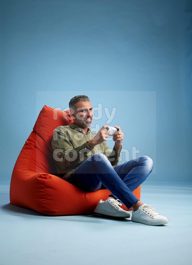 A man sitting on an orange beanbag and gaming with joystick