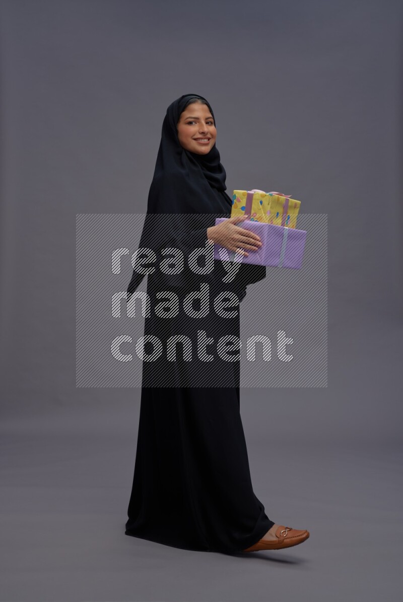 Saudi woman wearing Abaya standing holding gift box on gray background