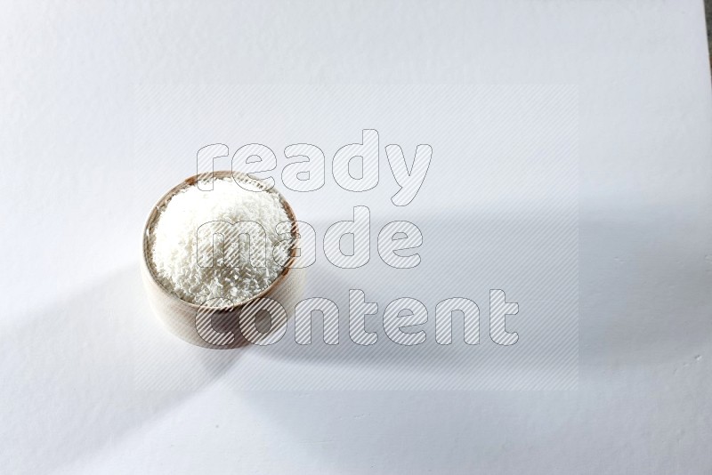A beige ceramic bowl full of desiccated coconut on a white background in different angles