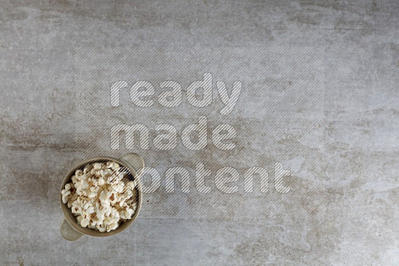 popcorn in a off-white handheld ceramic bowl on a grey textured countertop
