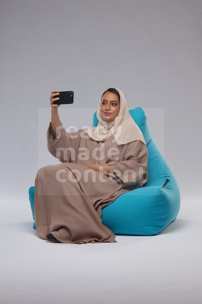 A Saudi woman sitting on a blue beanbag and taking selfie