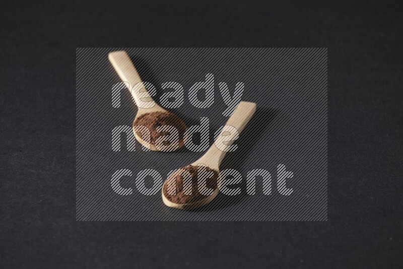 2 wooden spoons full of cloves powder on a black flooring