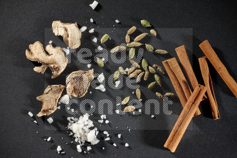 الزنجبيل والملح والهيل وأعواد القرفة على خلفية سوداء