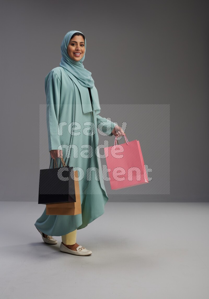 Saudi Woman wearing Abaya standing holding shopping bag on Gray background