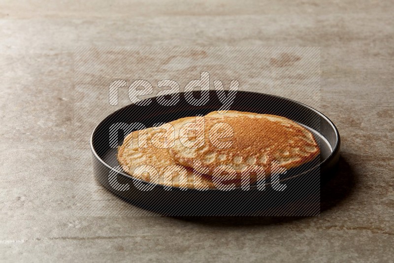 Two stacked plain pancakes in a black plate on beige background