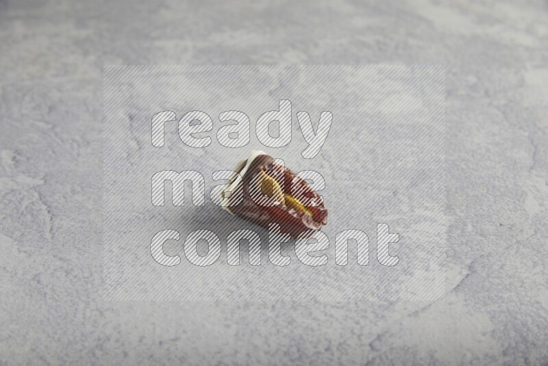 pistachio stuffed date covered with dark chocolate with white chocolate drizzle on a light grey background