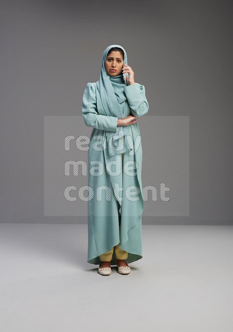 Saudi Woman wearing Abaya standing talking on phone on Gray background