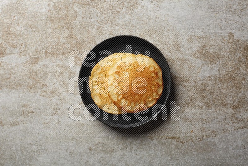 Two stacked plain pancakes in a black plate on beige background