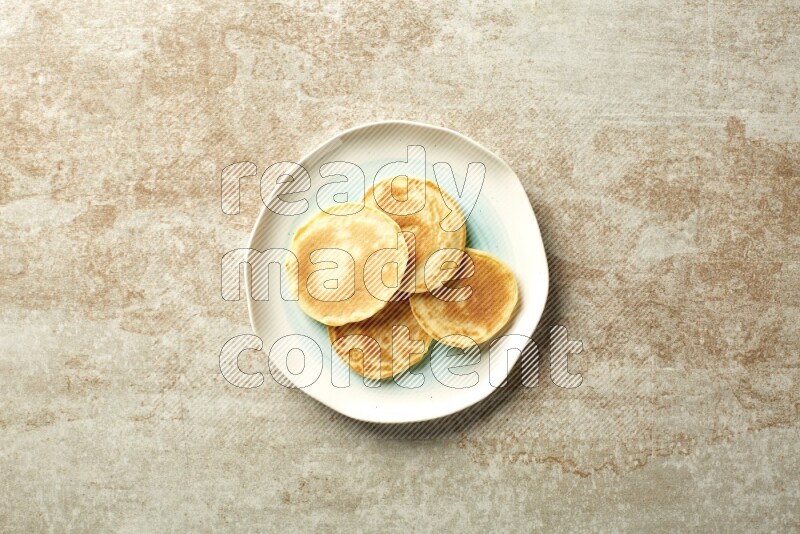 Four stacked plain mini pancakes in a bicolor plate on beige background