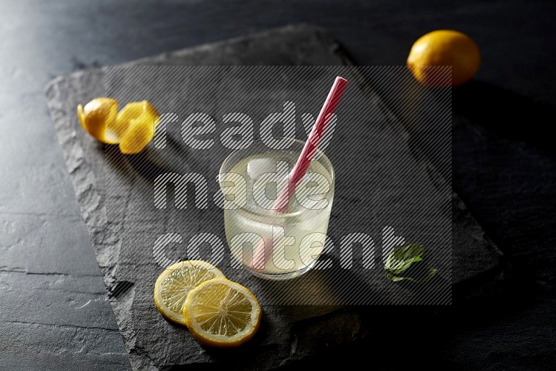 A glass of lemon juice with a straw on black background