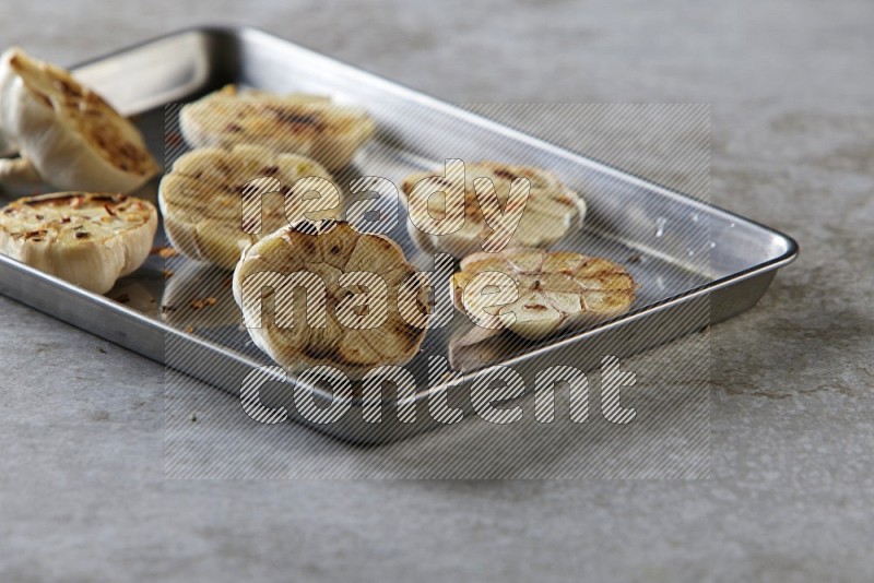 half's roasted garlic in a stainless tray on a grey textured countertop