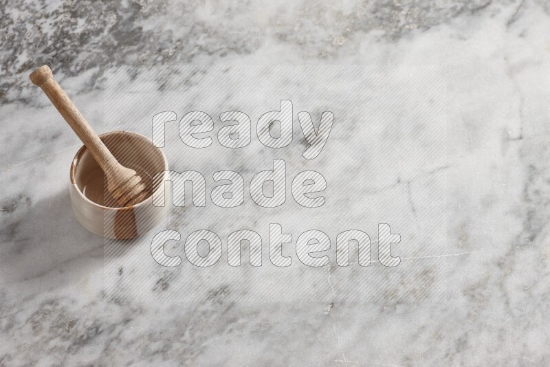 Beige pottery bowl with wooden honey dipper in it on grey marble background