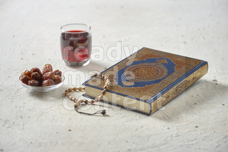 Quran with dates, prayer beads and different drinks all placed on textured white background