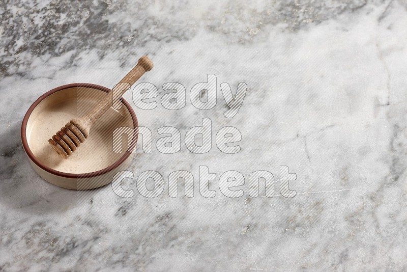 Beige Pottery oven bowl with wooden honey handle on the side with grey marble flooring, 65 degree angle