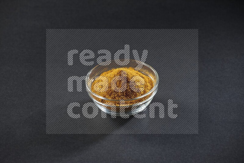 A glass bowl full of turmeric powder on black flooring