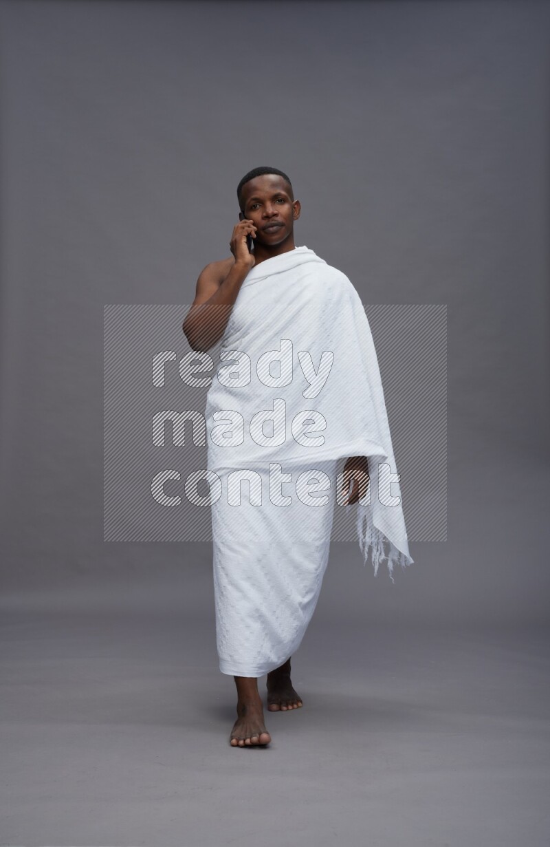 A man wearing Ehram Standing talking on phone on gray background