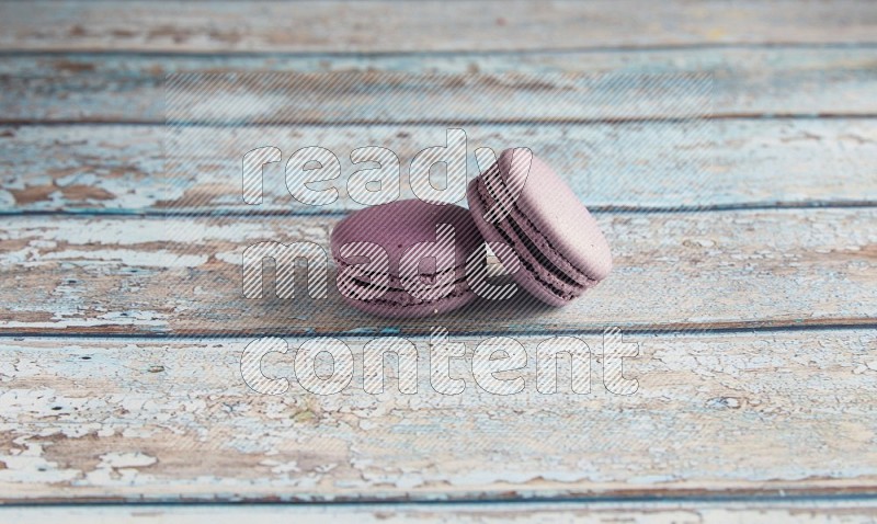 45º Shot of two Purple Blueberry macarons on light blue wooden background