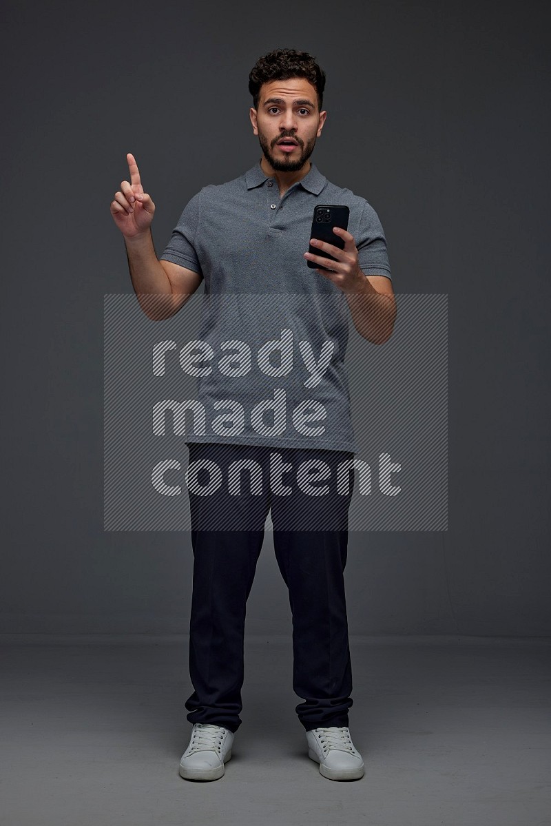 A man wearing casual standing and using his phone and making multi hand gestures eye level on a gray background
