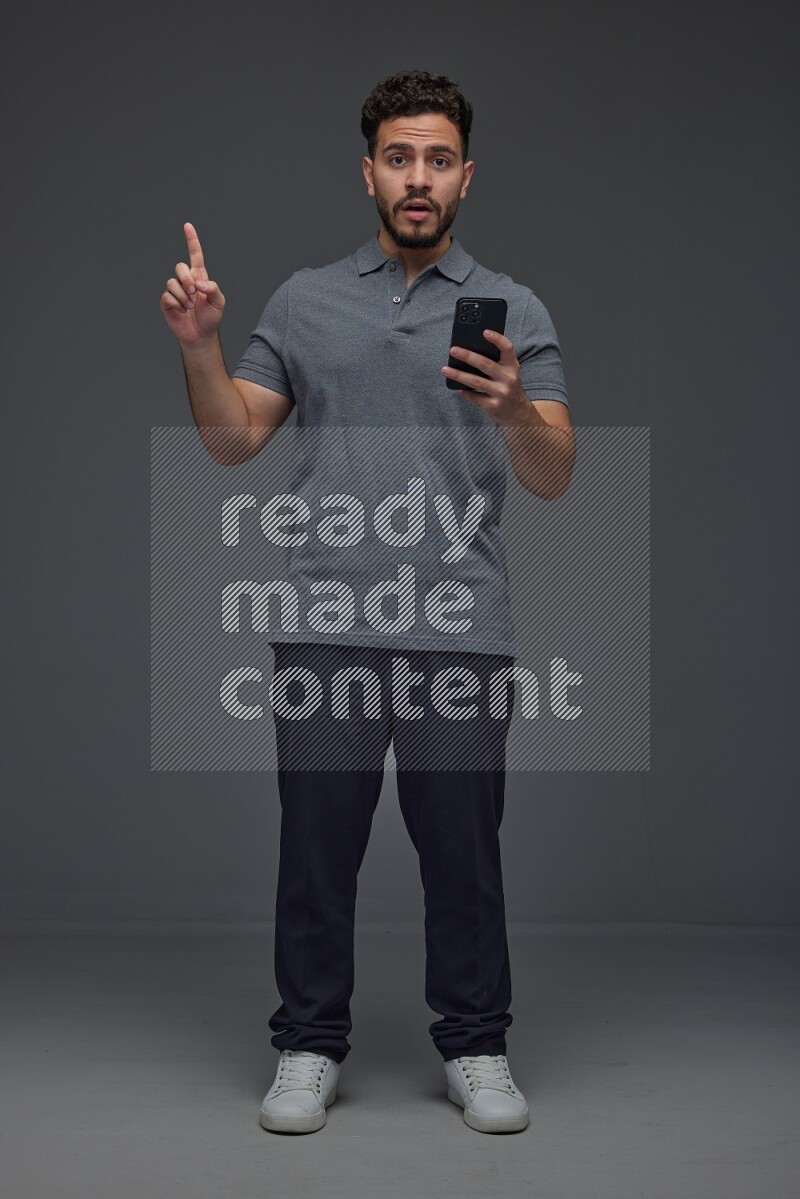 A man wearing casual standing and using his phone and making multi hand gestures eye level on a gray background
