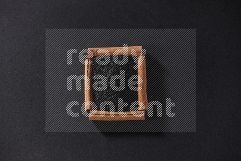 أربعة من أعواد القرفة مكونة شكل مربع بداخلها حبة البركة علي خلفية سوداء