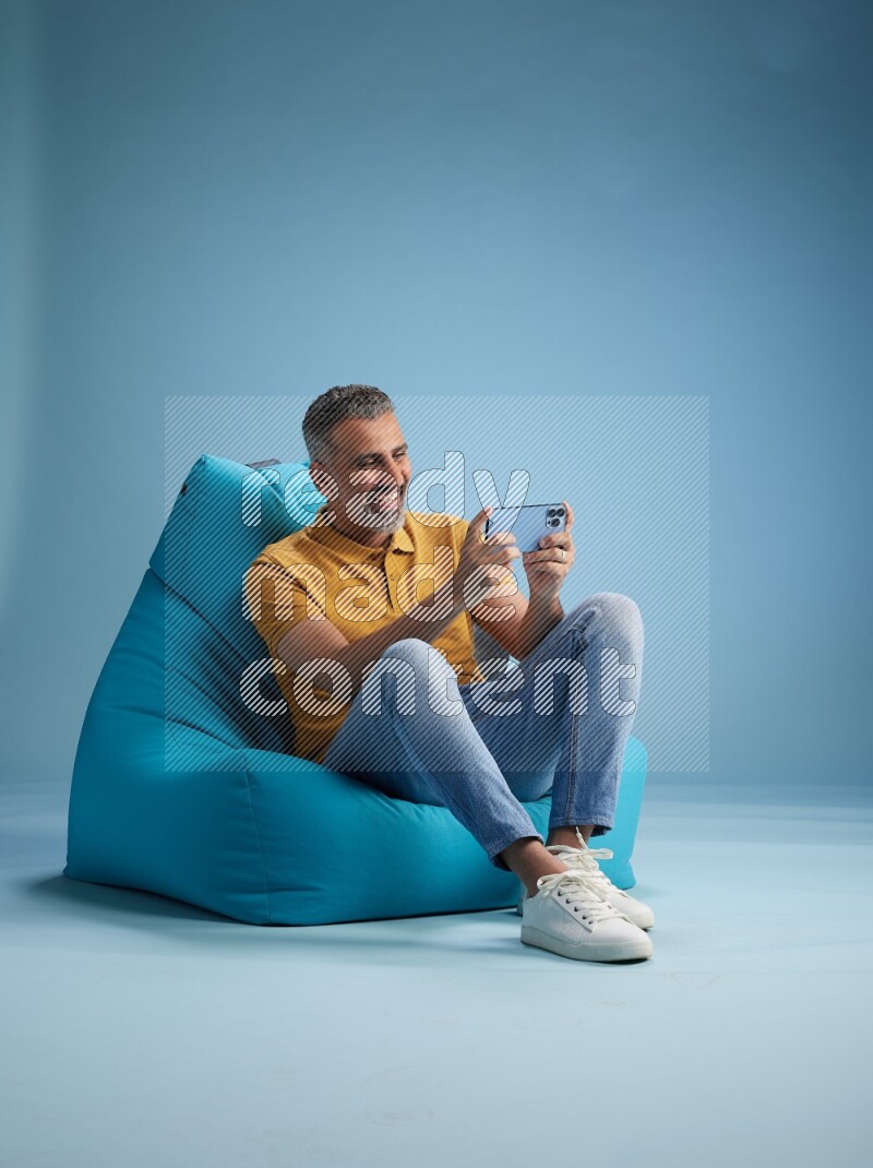 A man sitting on a blue beanbag and texting on phone