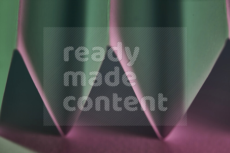 صورة مجردة مقربة تظهر طيات ورقية هندسية حادة بتدرجات اللون الأخضر والوردي