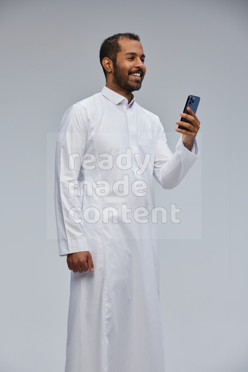 Saudi man wearing Thob standing texting on phone on Gray background