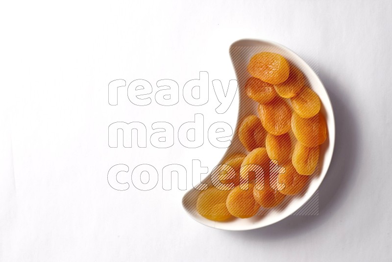 Dried apricots in a crescent pottery plate on white background
