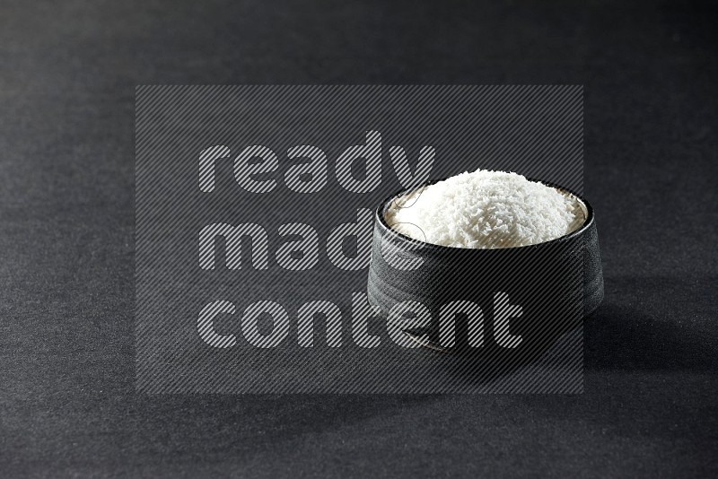 A black ceramic bowl full of desiccated coconut on a black background in different angles