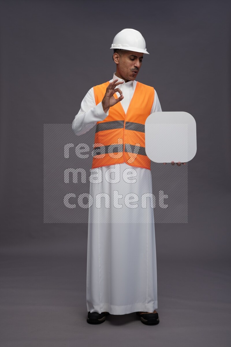 Saudi man wearing thob with engineer vest standing holding social media sign on gray background