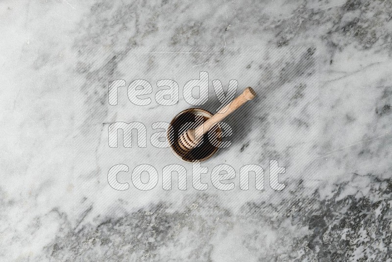 Brown Pottery Bowl with wooden honey handle in it, on grey marble flooring, Top View