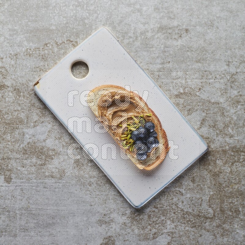 open faced peanut butter sandwich with blueberries and pistachio on a grey textured background