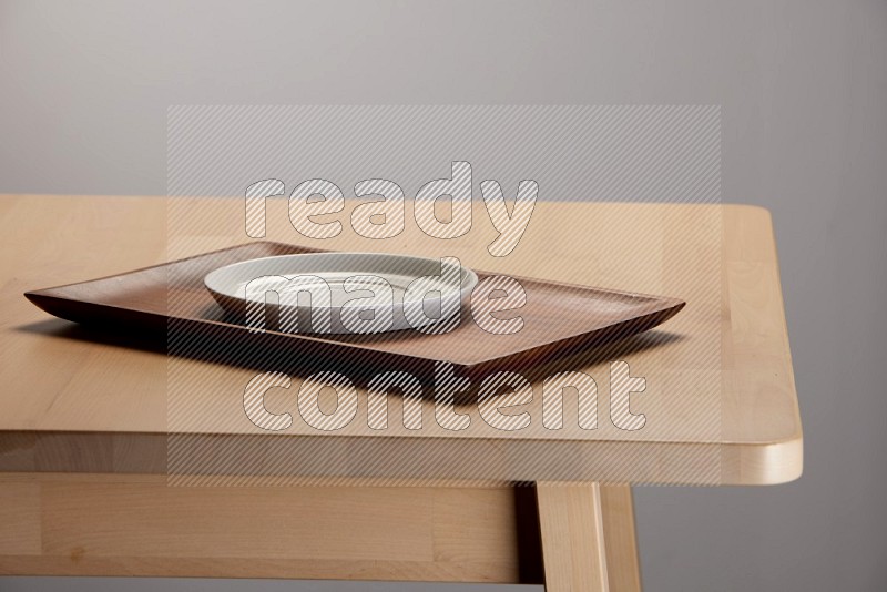 white plate on a rectangular wooden tray on the edge of wooden table