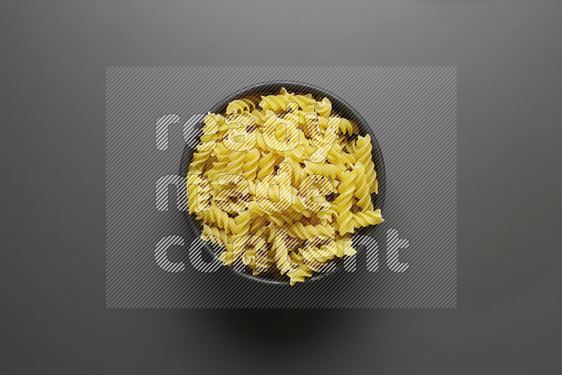 Fusilli pasta in a pottery bowl on grey background