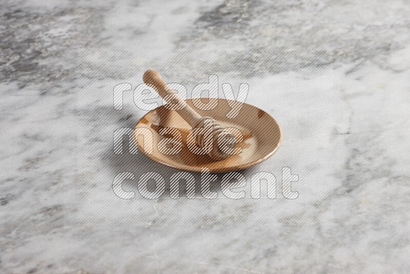 Multicolored pottery plate with wooden honey dipper in it on grey marble background
