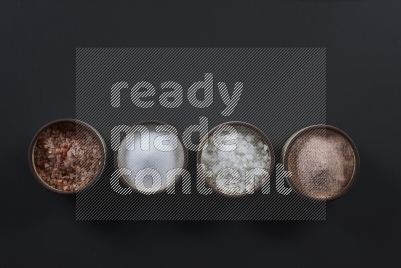 4 pottery bowls filled with himalayan salt and white salt on black background