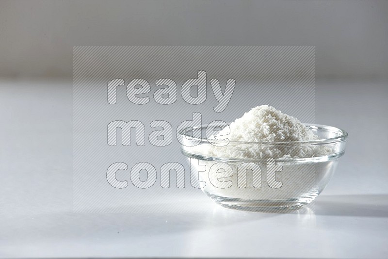 A glass bowl full of desiccated coconut on a white background in different angles