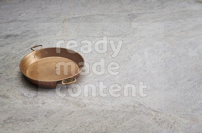 A Small Copper Pan On Grey Marble Flooring