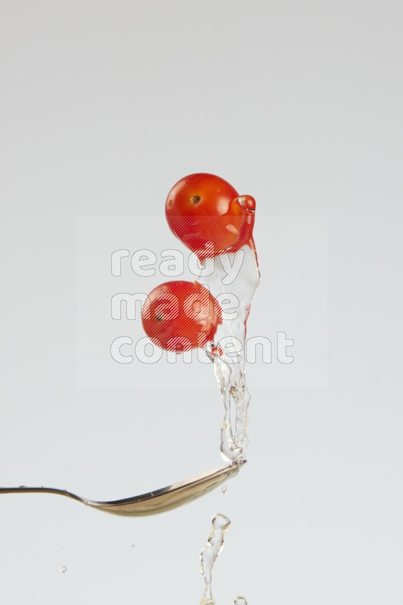 A metal spoon throwing two cherry tomatoes leaving a splash of water behind on a light blue background