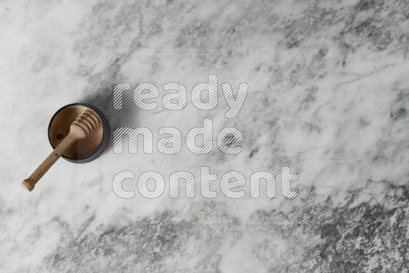 وعاء فخاري أسود مع ملعقة عسل خشبية بداخله على خلفية من الرخام الرمادي