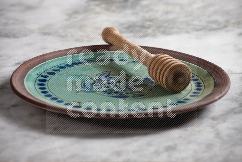 Decorative Pottery Plate with wooden honey handle in it, on grey marble flooring, 15 degree angle