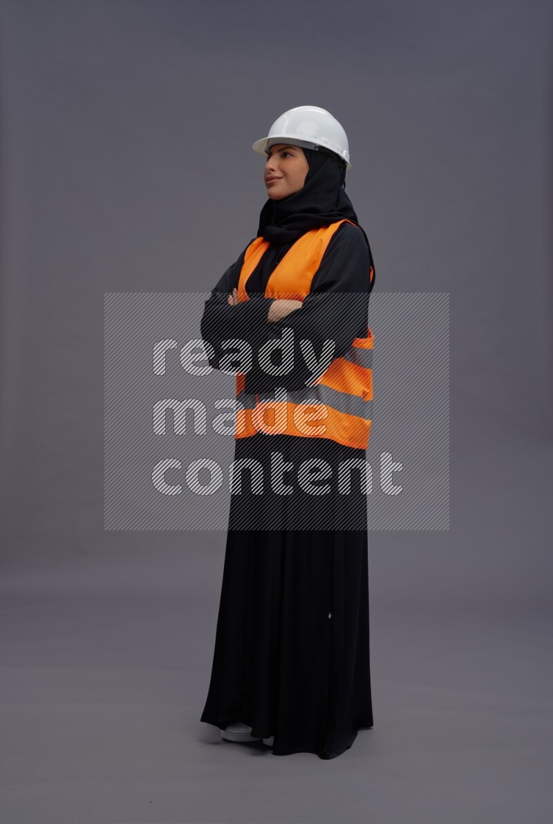 Saudi woman wearing Abaya with engineer vest standing with crossed arms on gray background