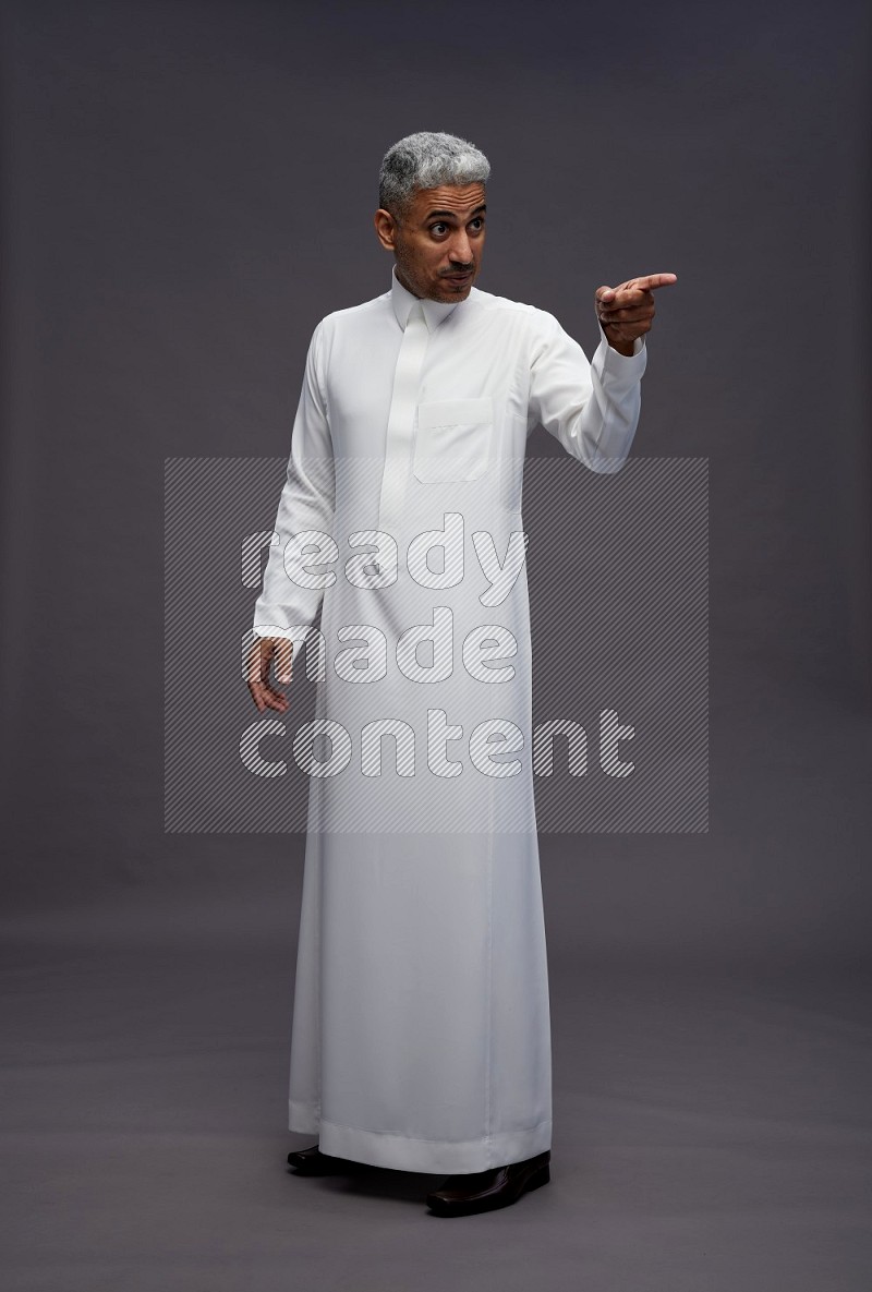 Saudi man wearing thob standing interacting with the camera on gray background