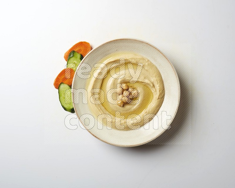 Hummus in a pottry plate garnished with roasted chickpeas on a white background