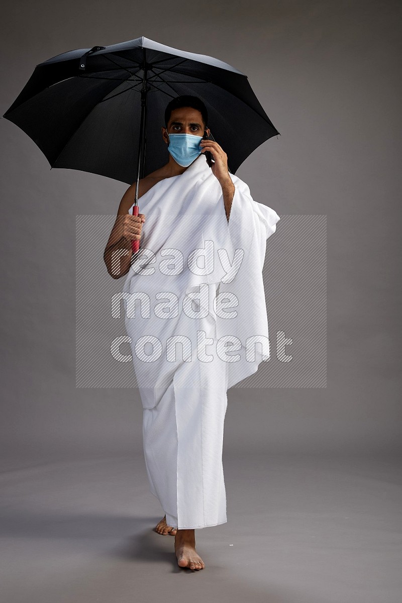 A man wearing Ehram and mask Standing holding umbrella on gray background on gray background