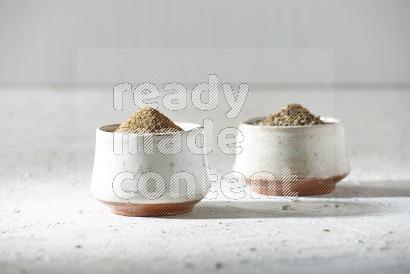2 beige bowls full of cumin seeds and powder on a textured white flooring