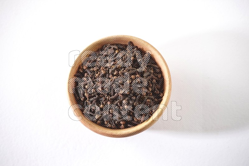 A wooden bowl full of cloves on a white flooring